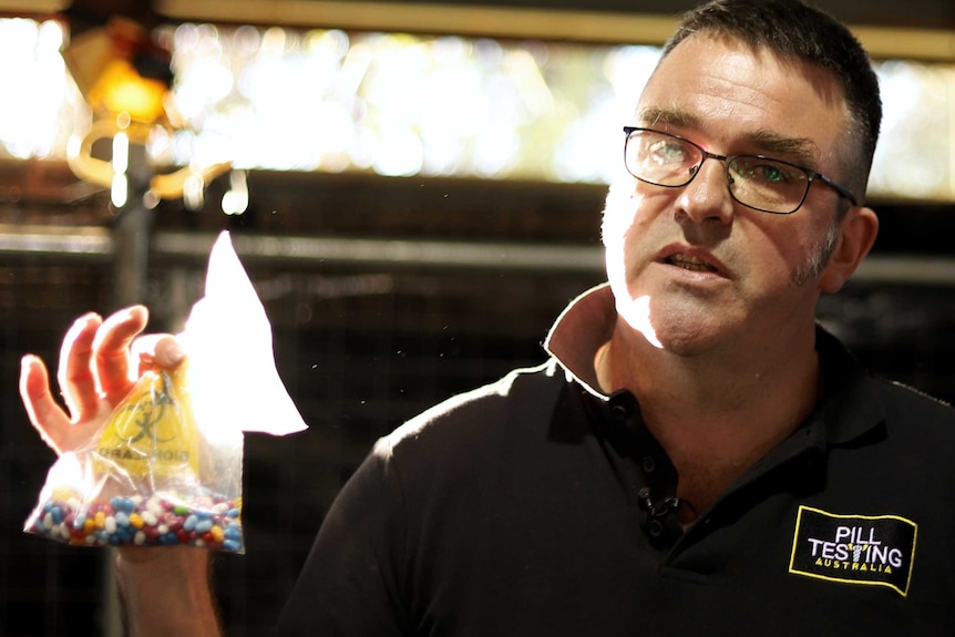 A man holds a medical waste bag, with a lot of colourful pills inside it.