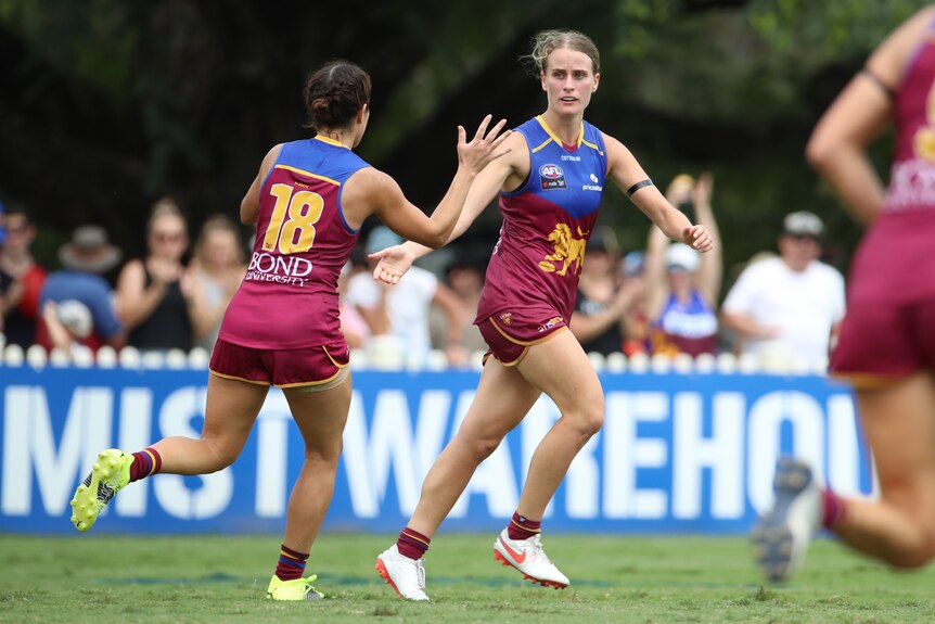 An AFLW player runs away after kicking a goal, holding her hand out to high-five an approaching teammate.