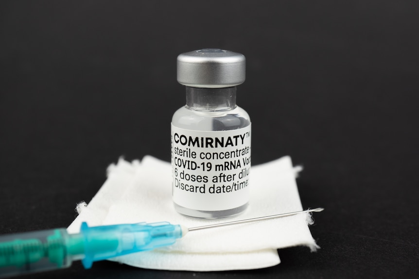 Small glass vial of Pfizer COVID-19 vaccine with accompanying needle.