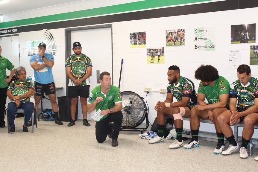 Townsville Blackhawkes rugby coach crouches down, surrounded by the team, to give a team talk