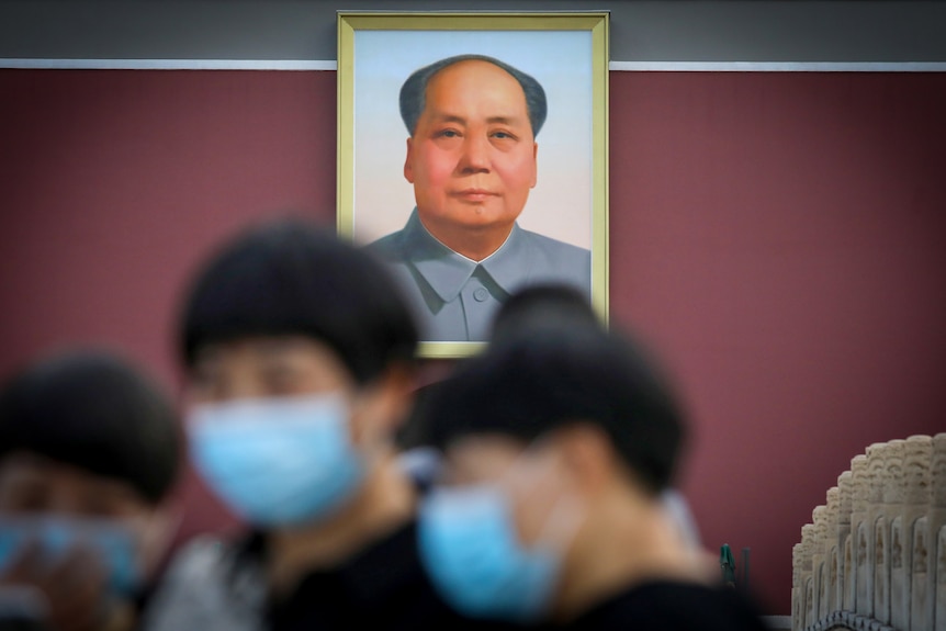 A portrait of Chairman Mao with masked people in the foreground