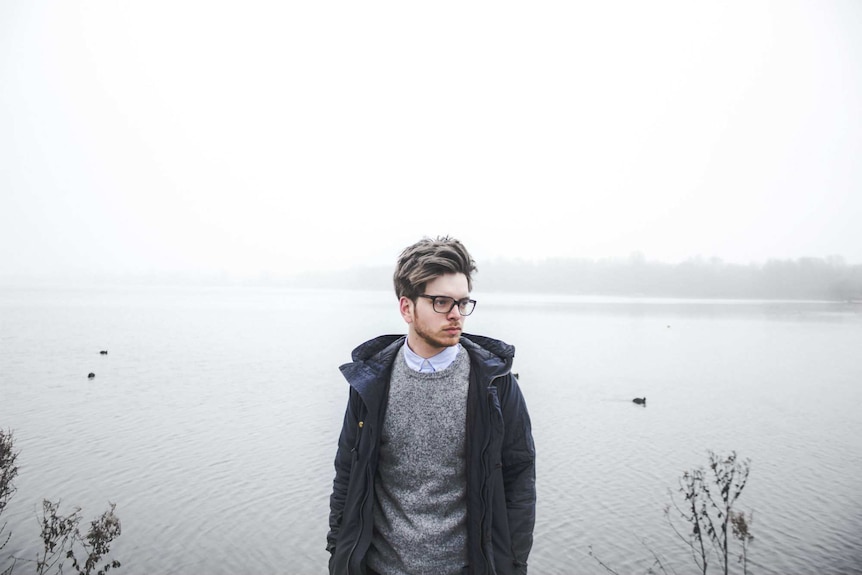 A man wearing a grey sweaters stands on the edge of a lake, an example of a classic men's casual wardrobe look