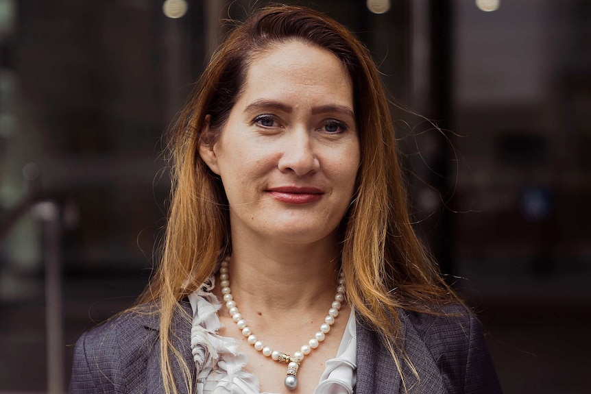 A headshot of a woman in a grey business suit and white top in front of a building.