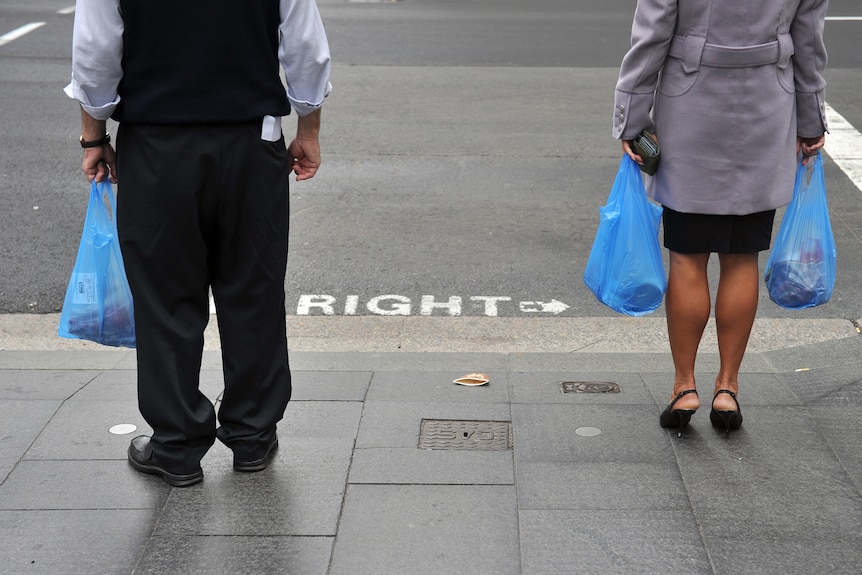 a man holding a plastic bag standing next to a woman holding a plastic bag