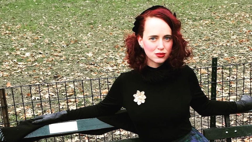 Tara Isabella Burton sitting on a park bench, wearing a beret and blue and green tartan skirt.