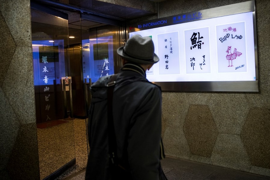 A man in a hat looks at an information board in Tokyo, Japan.