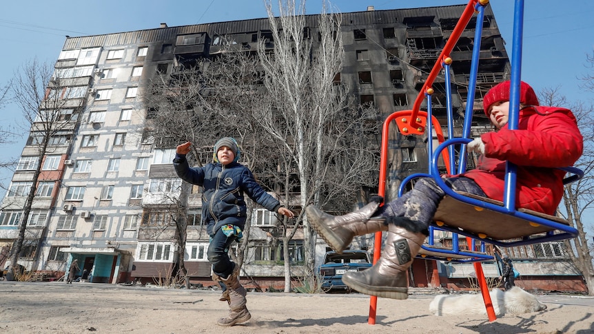 Children play in front of a building damaged in fighting.