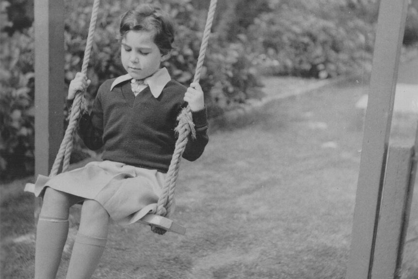 Black and white photo of a young child on a swing in the backyard.