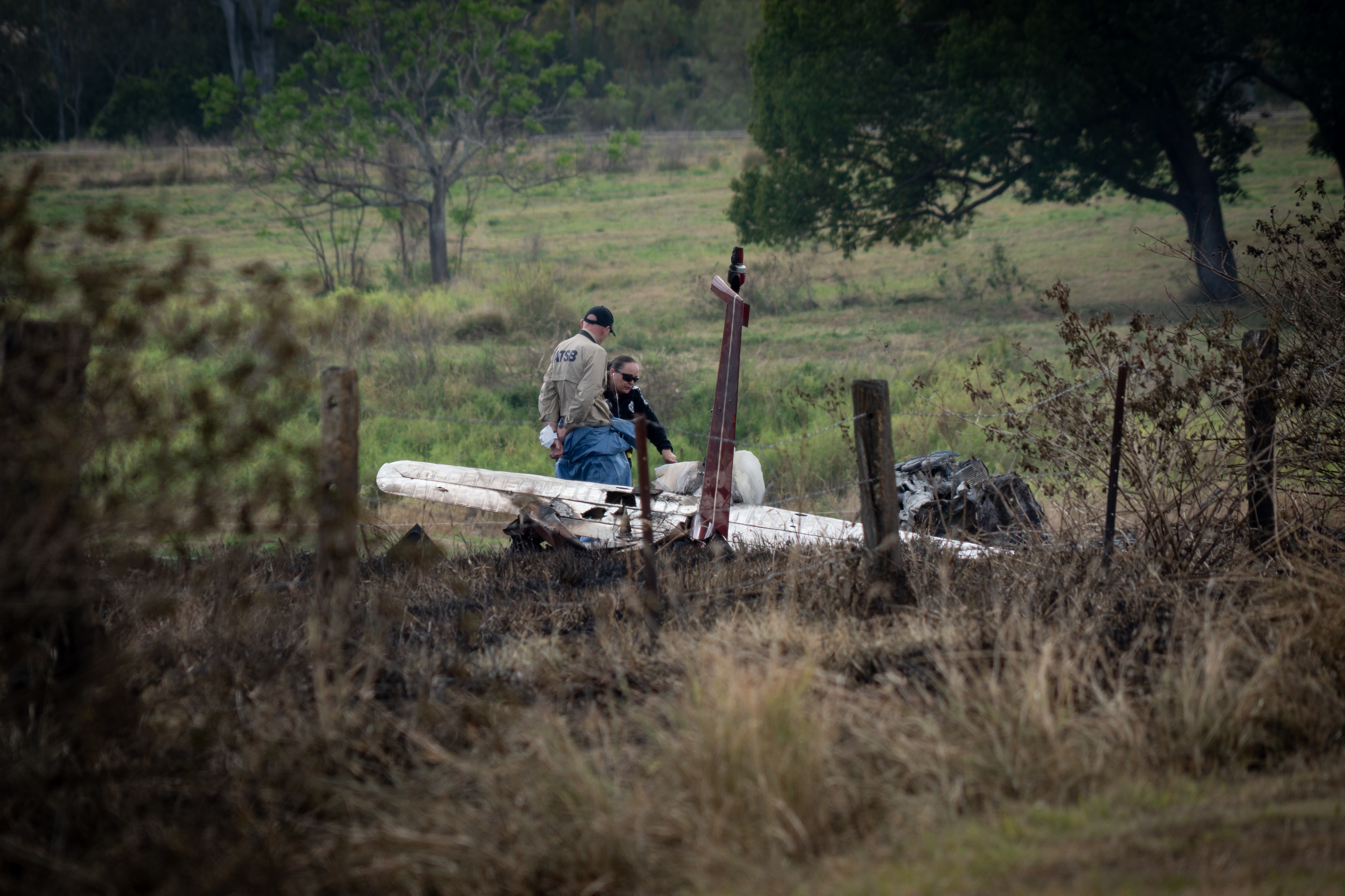 Two air crash investigators examining a crashed light plane in a field.