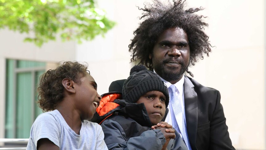 An Aboriginal man sits in a courtyard with his two sons