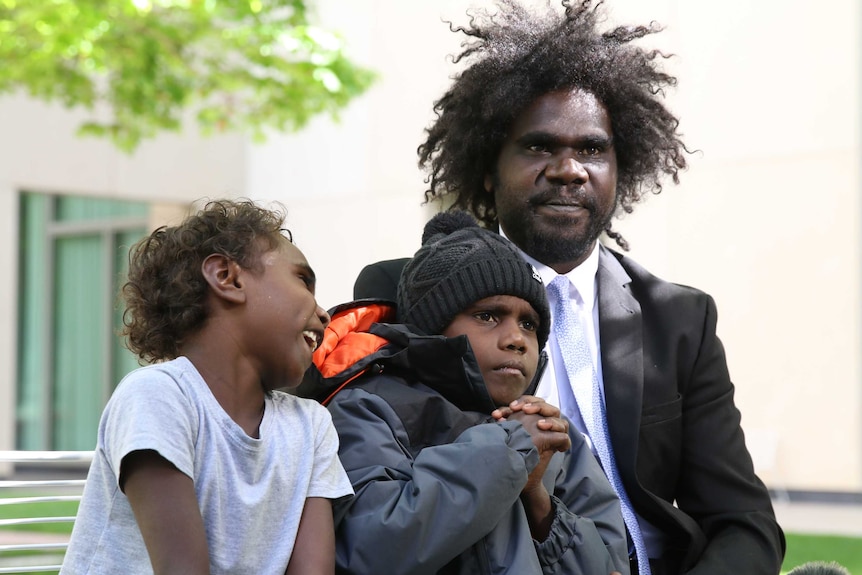 An Aboriginal man sits in a courtyard with his two sons