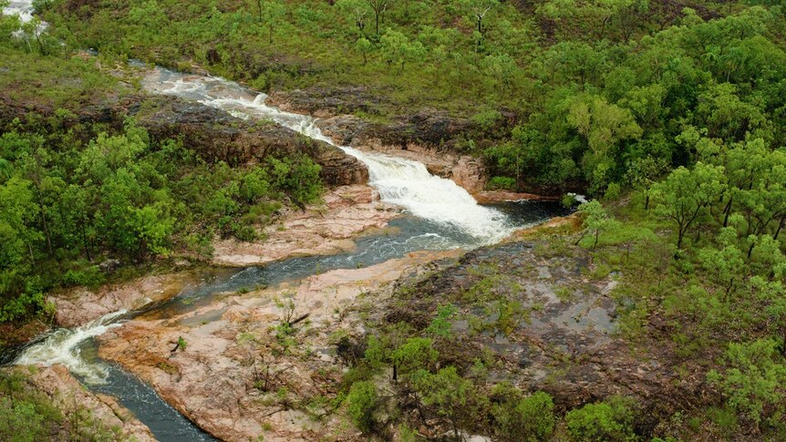 An aerial shot of a cascading waterfall, surrounded by green bush land.