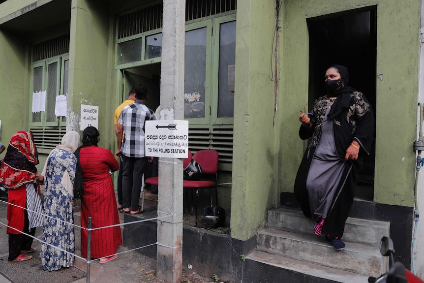 Sri Lankans queue out side a polling station as a woman exits from another door.
