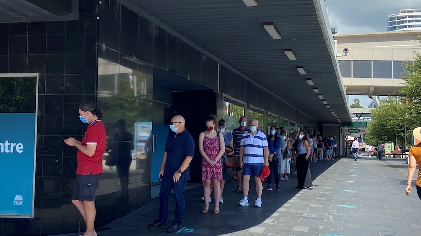 People queue with masks on outside a building