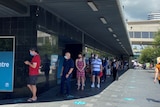 People queue with masks on outside a building