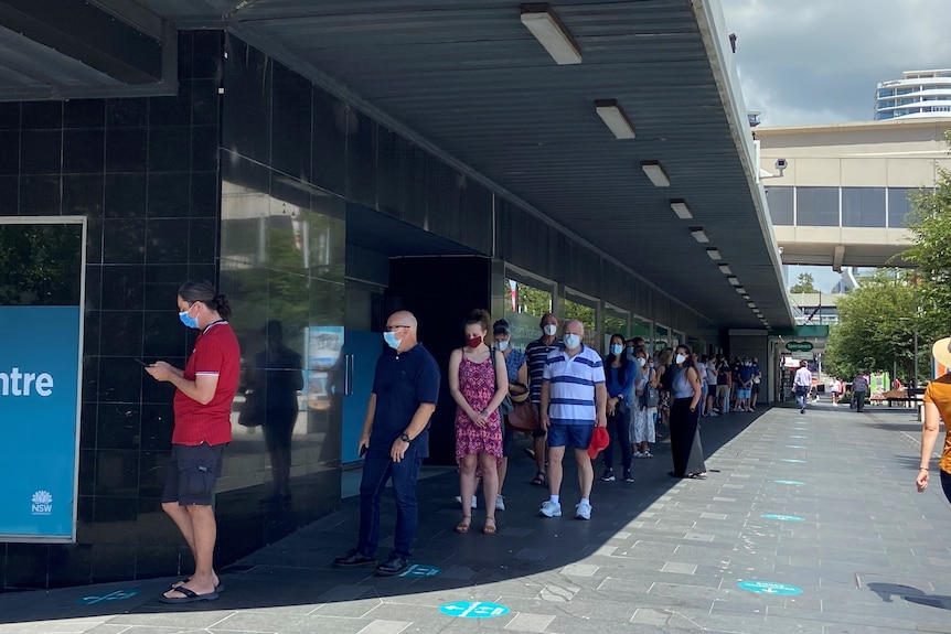 People queue with masks on outside a building