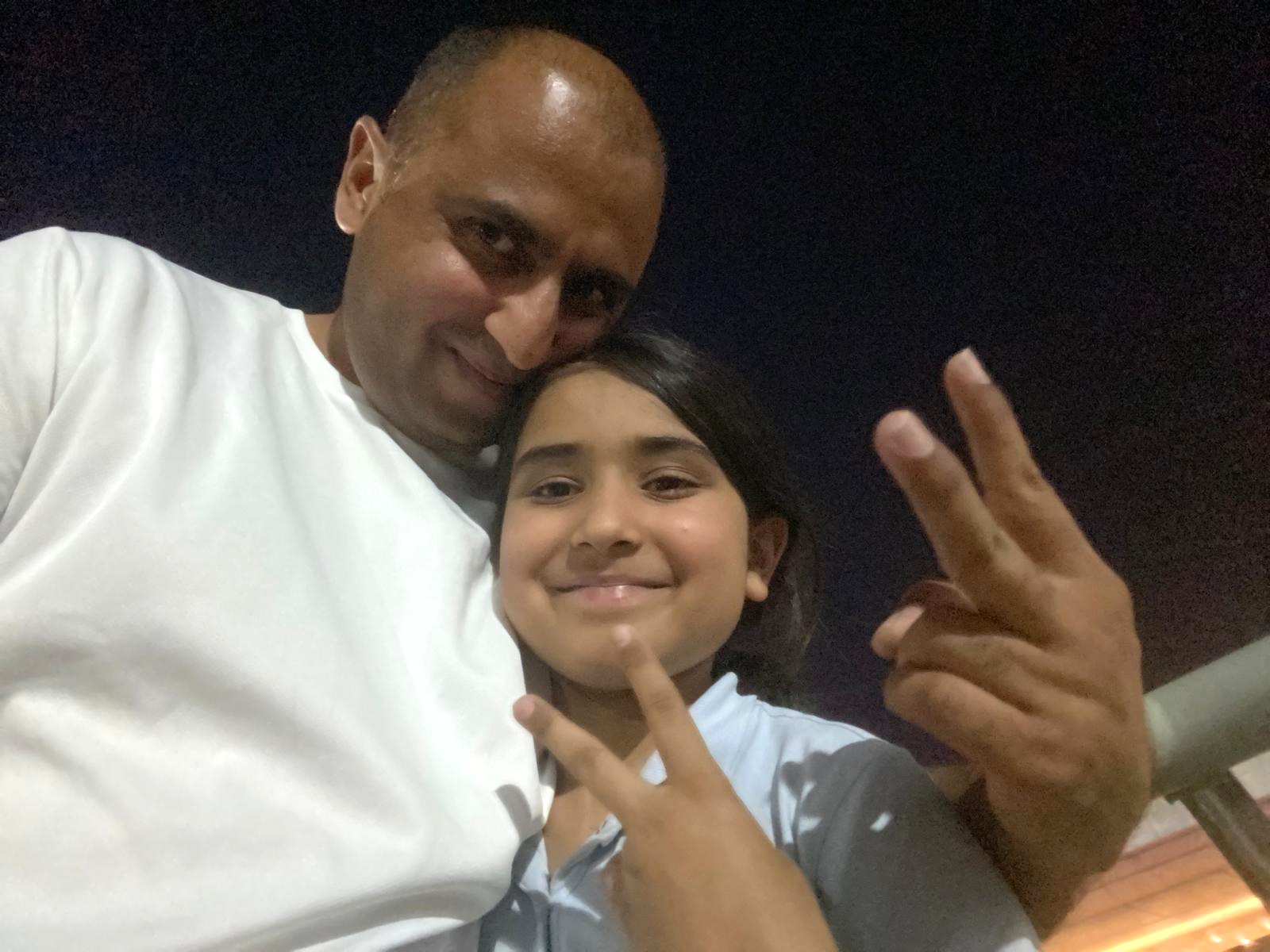 Selfie of a man hugging his young daughter and forming finger signs.