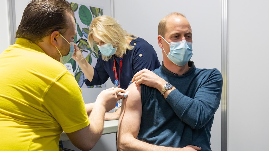 Prince William, wearing a mask, is injected in his right arm.