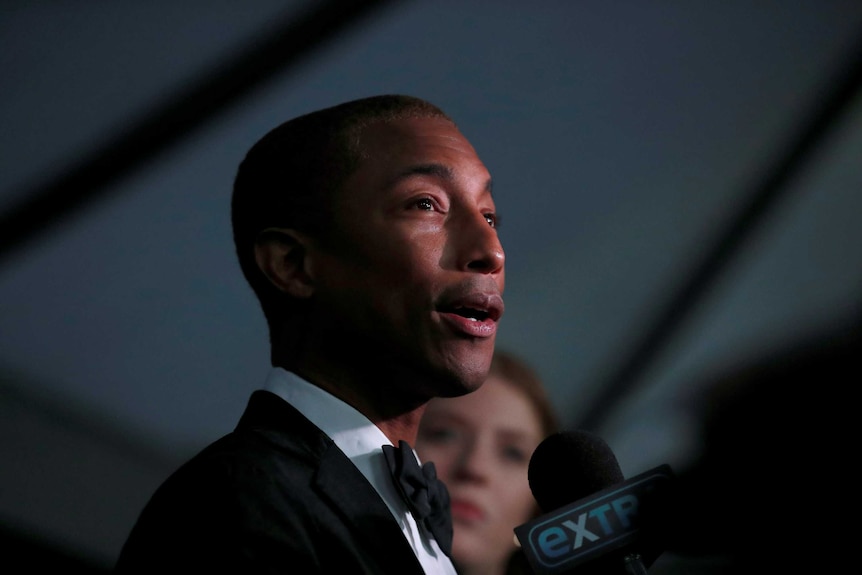 Pharrell Williams talks into a microphone wearing a suit.