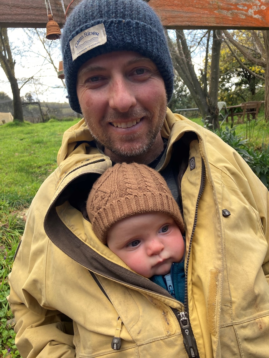 Man wearing beanie with young baby tucked inside jacket. 