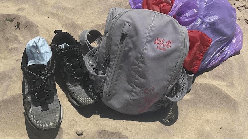 A pair of shoes and a backpack lying on some sand.