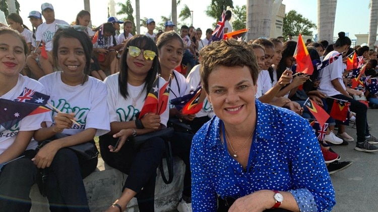 Barker kneeling in front of group of smiling Timorese teenagers holding flags.