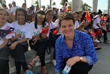 Barker kneeling in front of group of smiling Timorese teenagers holding flags.