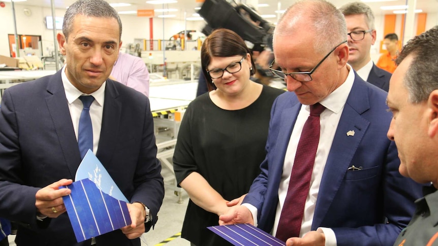 Three government ministers examine solar panel materials.