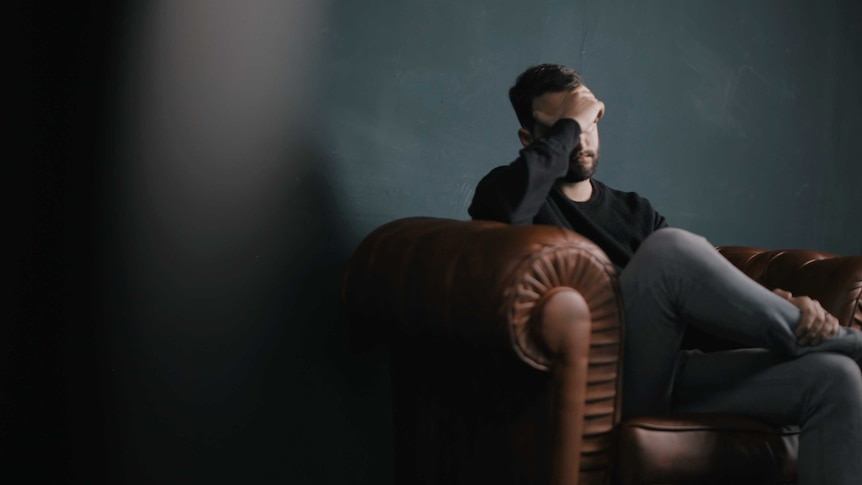 Man sitting on couch with his head in his hands