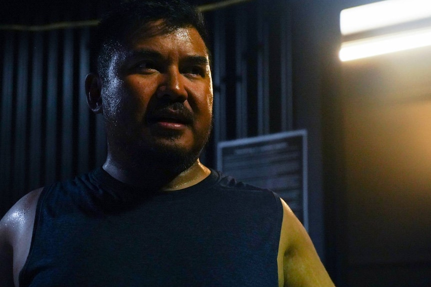 Man sweating in gym, gold light in background 