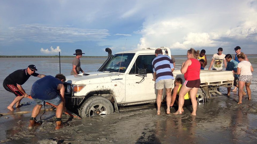 Beachgoers try to dig out a ute stuck in shallow waters off Broome.
