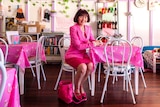 A woman wearing all pink sits in a cafe with pink table clothes.