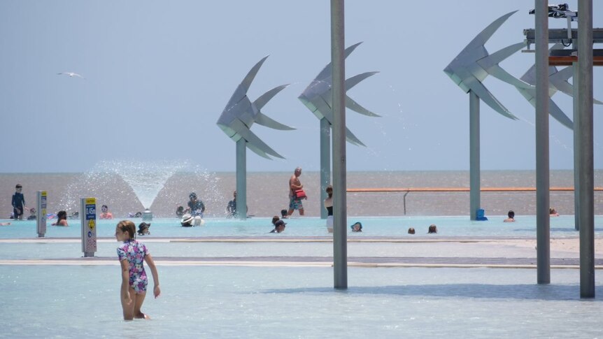 Children and adults swimming in the Cairns lagoon, in front of giant metal fish statues