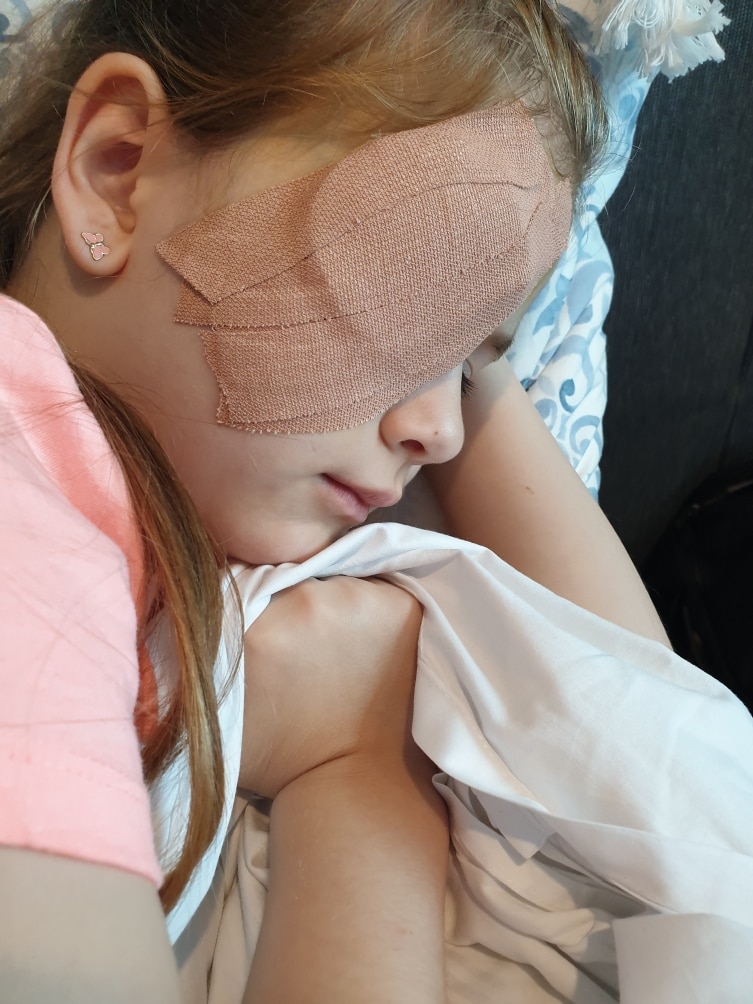 A young girl lying down, with bandages over her right eye