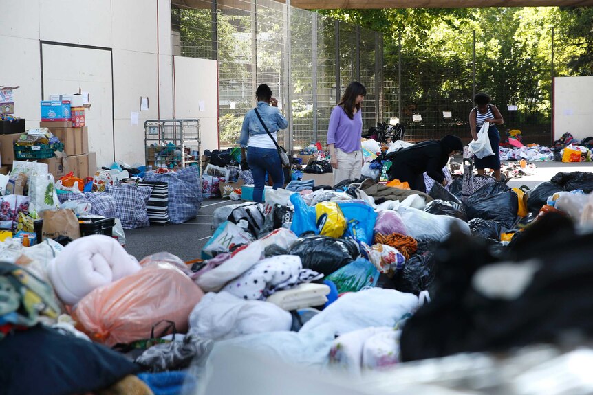 People stands amongst piles of bags of items donated to the homeless.