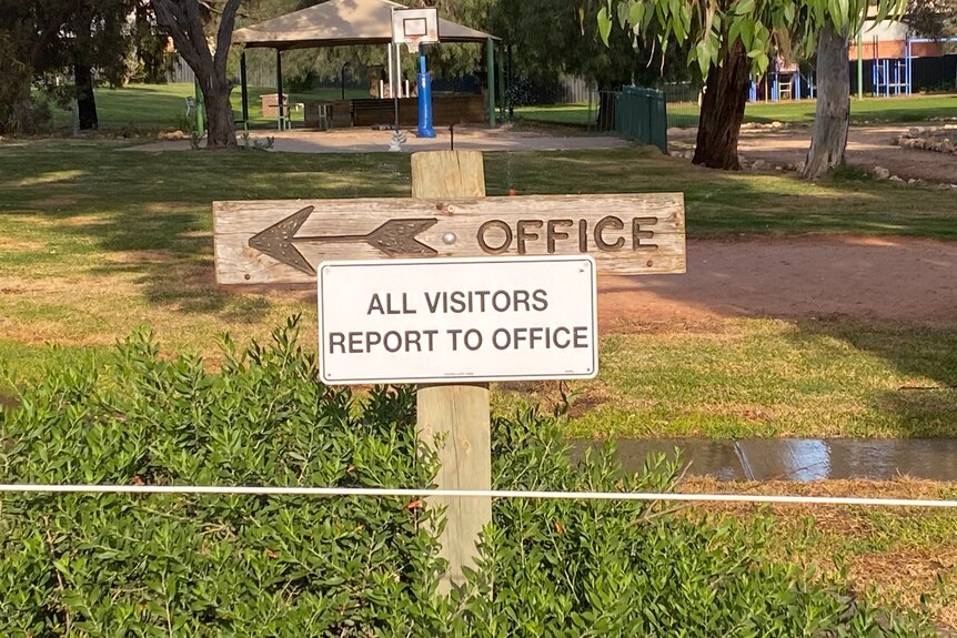 A wooden sign with an arrow points left, it reads "office, all visitors report to office."