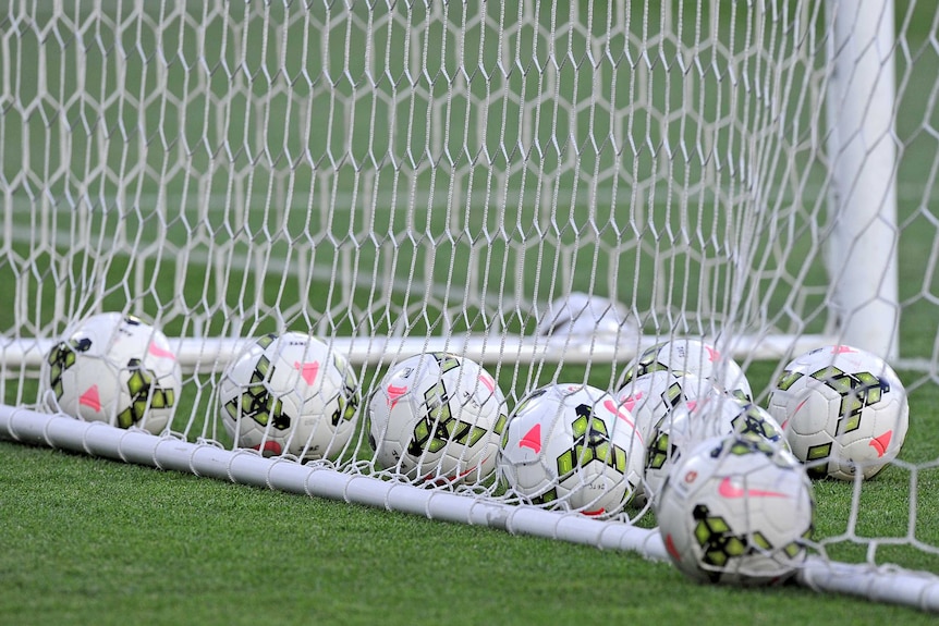 Several soccer balls lie inside the goal posts.