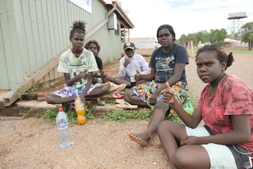 Members of the Maningrida community sit on the ground in the town's streets.