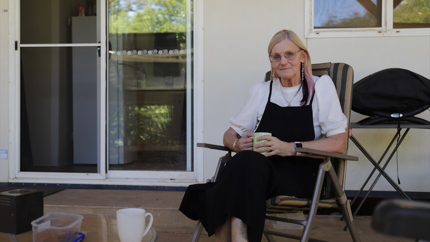 a woman sitting in a chair outside a house holding a cup of tea