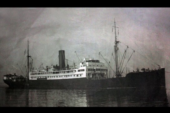 Wide black and white shot of an old navy ship on water.