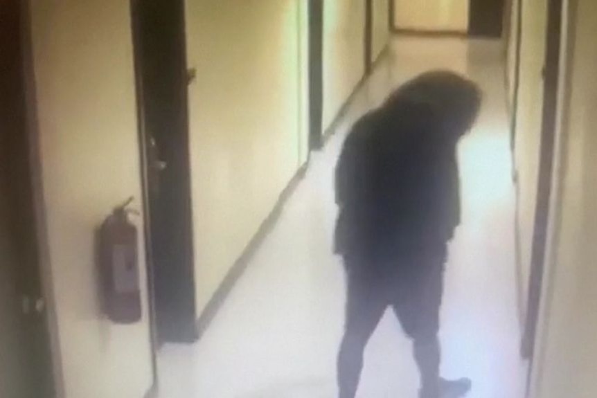 CCTV vision of a hooded figure walking down a hotel corridor.