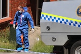 Man in forensics overalls exiting a house near police vehicle.