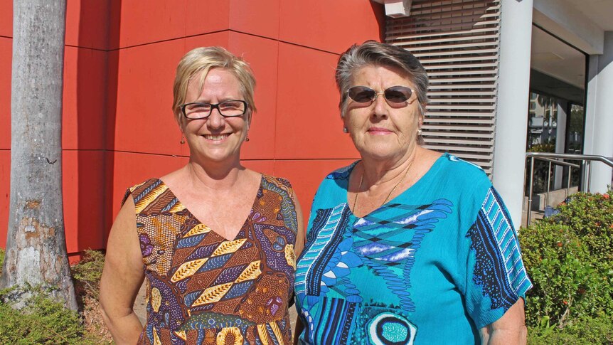 Two middle-aged women in colourful tops stand in front of a building on a sunny day in Darwin.