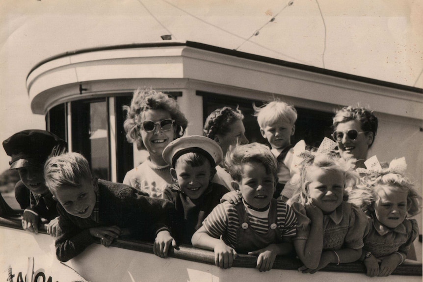 Women and children dressed in 1940s garb lean over the edge of the Tacoma tuna boat. The Tacoma's life saving ring can be seen.