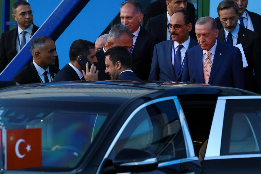 Tayyip Erdogan standing in a group of men in suits, about to get into a car