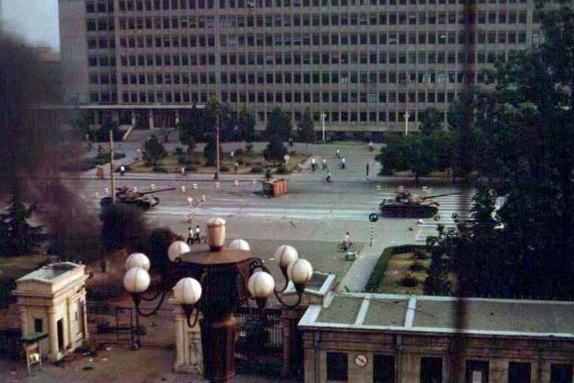 A car burns as tanks roll down Chang An Boulevarde en route to Tiananmen Square