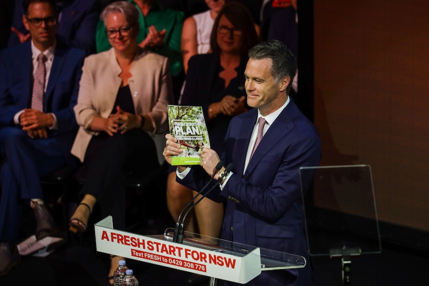 a man holding a document at an indoor public rally