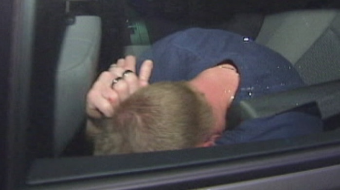 Adrian Bayley covers his face in the back seat of a car