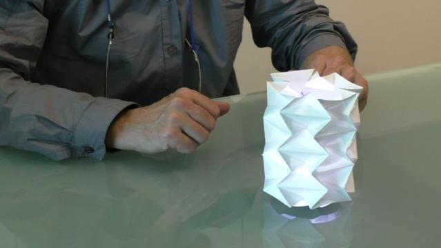 Hands sit beside paper folded into a complex cylinder shape