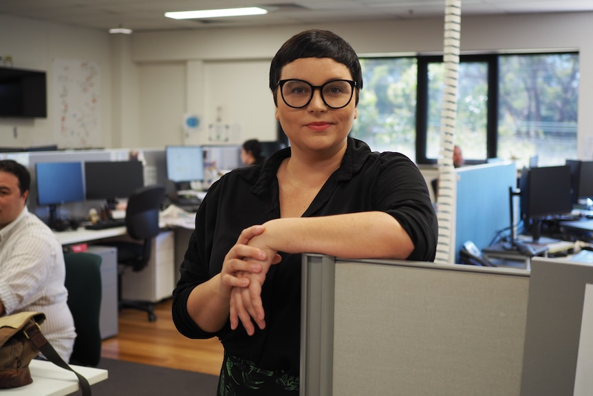 A young woman with glasses and short dark hair in a office setting. 